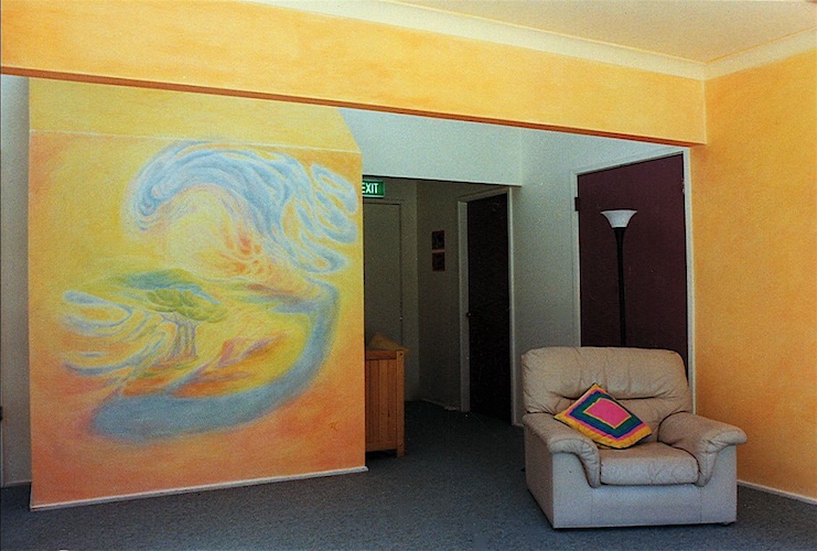 a mural of trees by a stream beneath a sunrise on a wall in a living room